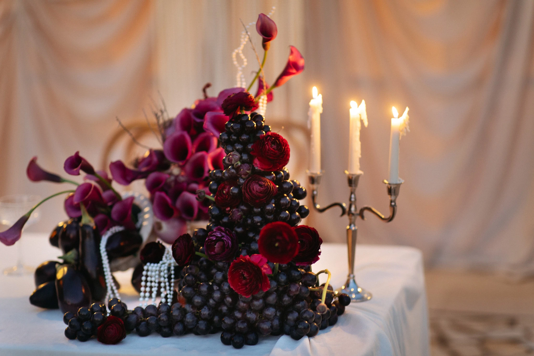Flottie wedding decor and organisation: dramatic tablescape featuring rich burgundy floral arrangements, dark grapes, eggplants, and a silver candelabra for the Shades of Burgundy project