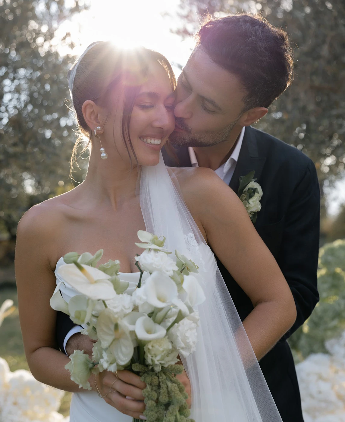 Flottie wedding decor and organisation: romantic couple embracing outdoors amidst white floral arrangements and refined table settings for the Where Light Lingers wedding project