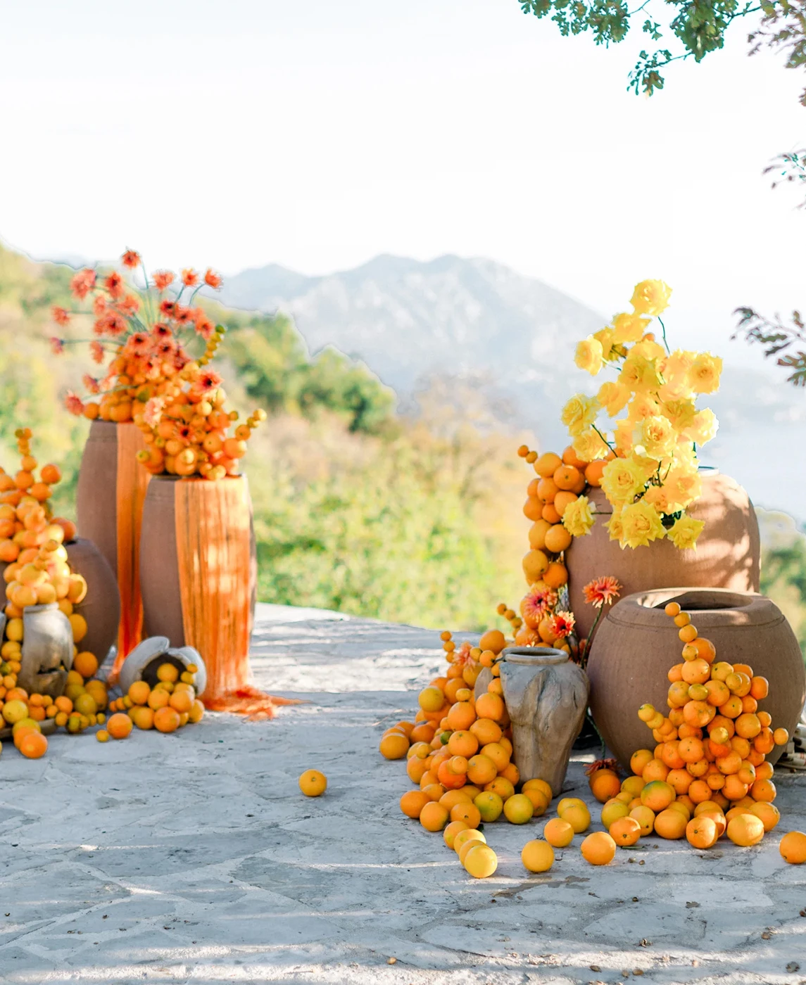 Flottie wedding decor and organisation: vibrant outdoor ceremony and terrace styling featuring dramatic terracotta vases overflowing with fresh oranges and bright yellow florals for the Citrus Muse project