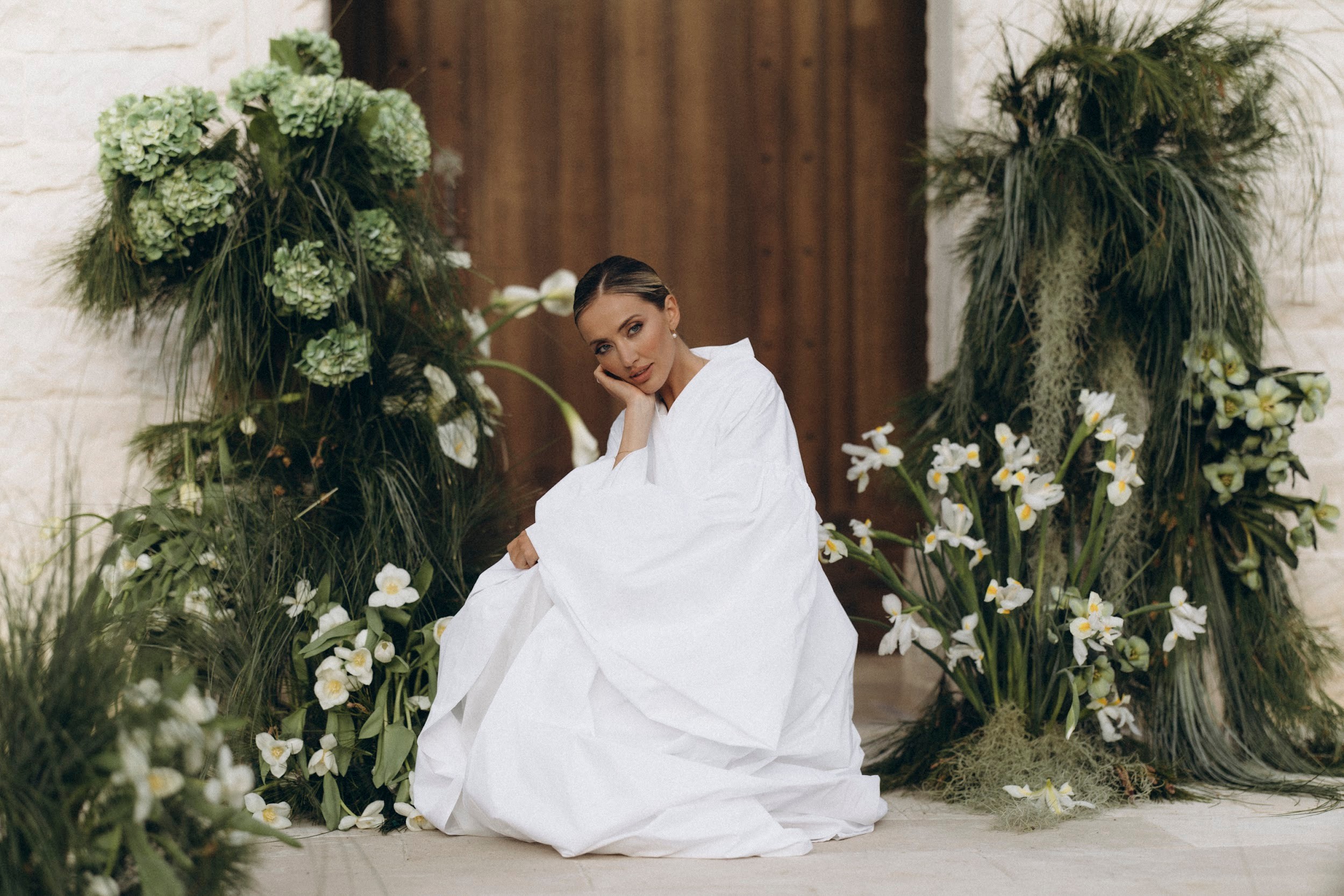 Flottie wedding decor and organisation: elegant bride in a white gown sitting amidst lush green installations and white floral arrangements for the Soul Vibes wedding project