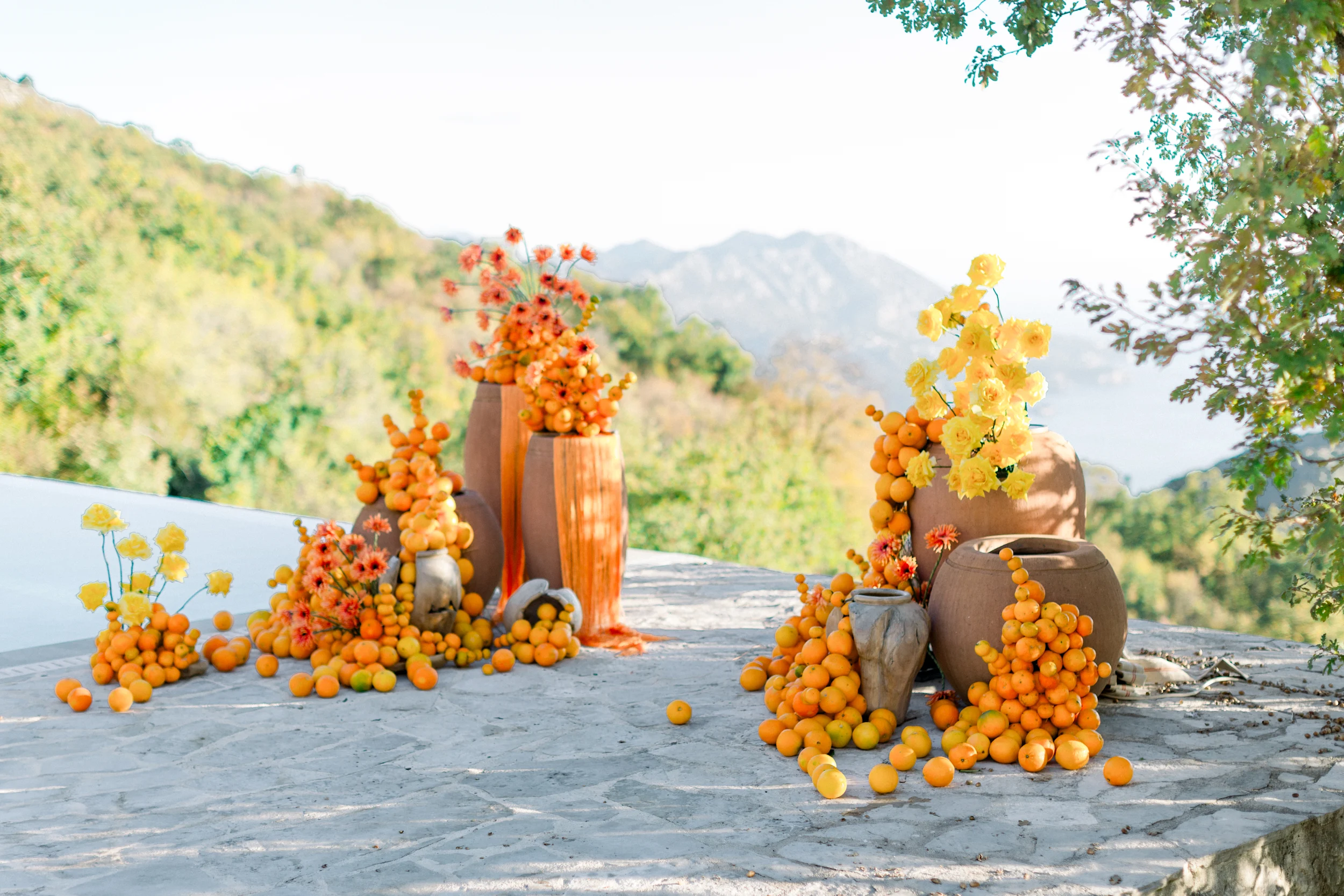 Flottie wedding decor and organisation: vibrant outdoor ceremony and terrace styling featuring dramatic terracotta vases overflowing with fresh oranges and bright yellow florals for the Citrus Muse project